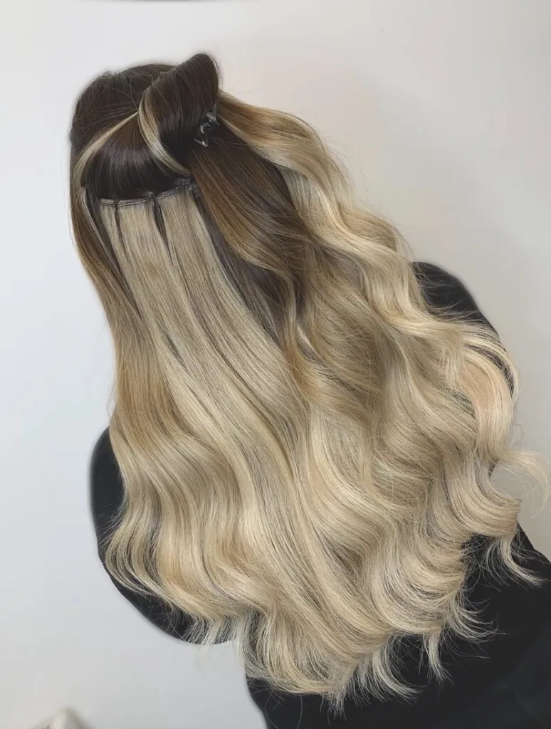Blonde weft hair extensions blended through darker hair and styled in soft waves at Esther Alexander