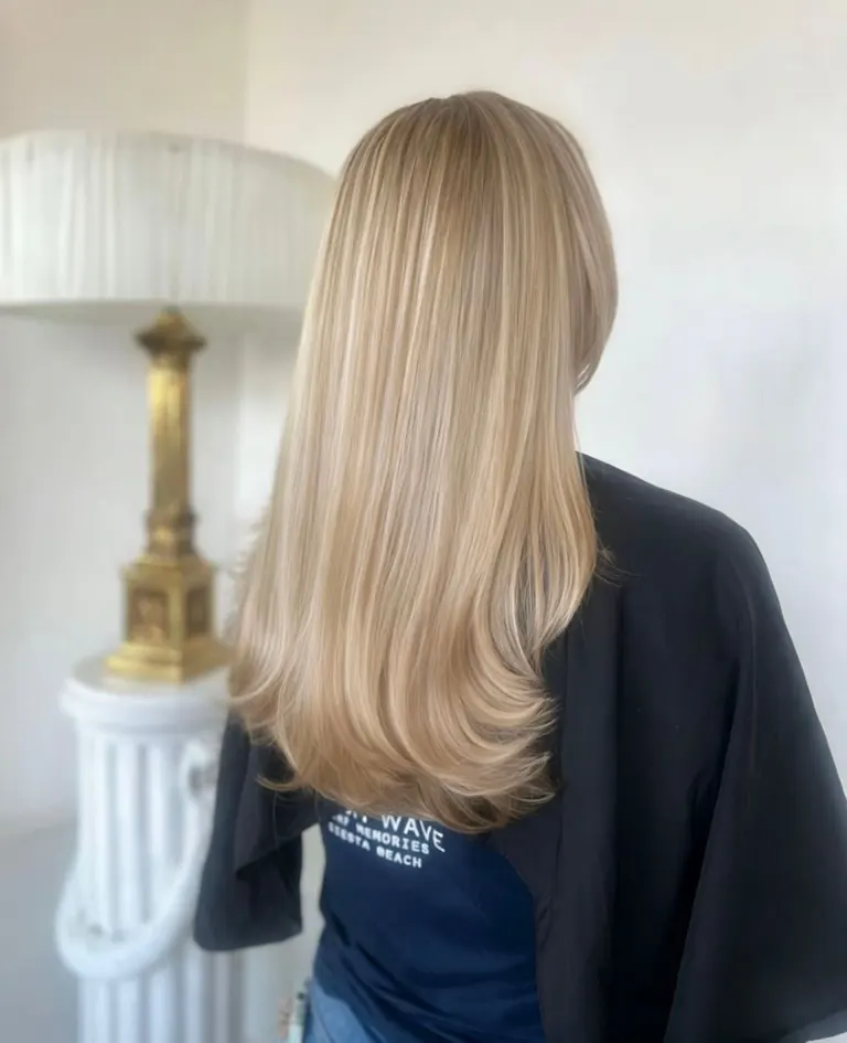 Long layered blonde hair with soft movement and a blow-dried finish